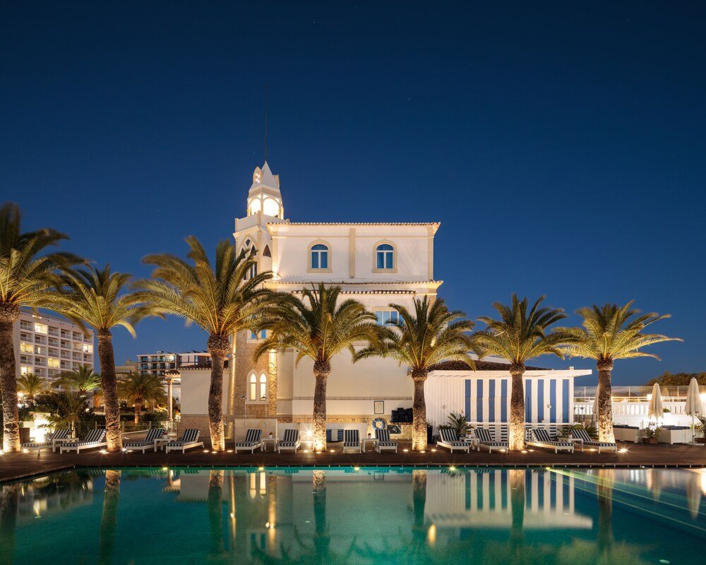 Hotel with a pool, palm trees and a lit tower