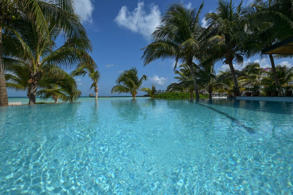 Clear blue pool surrounded by palm trees at Casa del Jaguar Beach Hotel