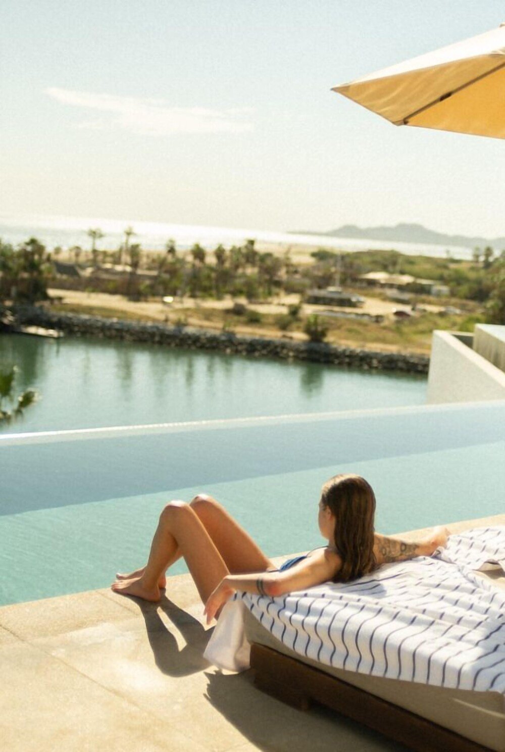 Persona descansando en un camastro junto a la piscina con vista a la playa
