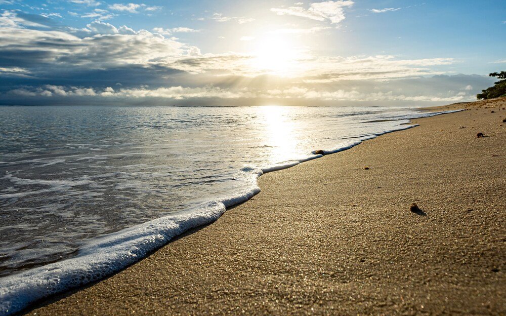 Playa bajo un cielo despejado con el sol reflejado en el agua