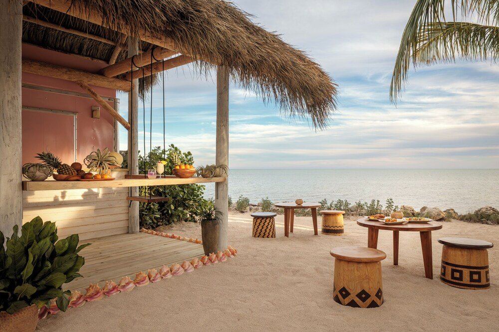 Patio junto a la playa con muebles de madera y techo de palma