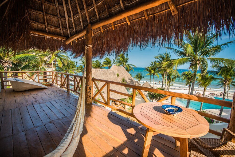 Wooden deck with a thatched roof overlooking a palm-lined beach