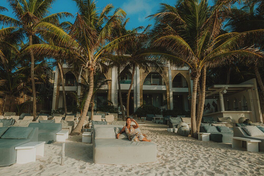 Zona de descanso junto a la playa con sillas blancas y una palmera