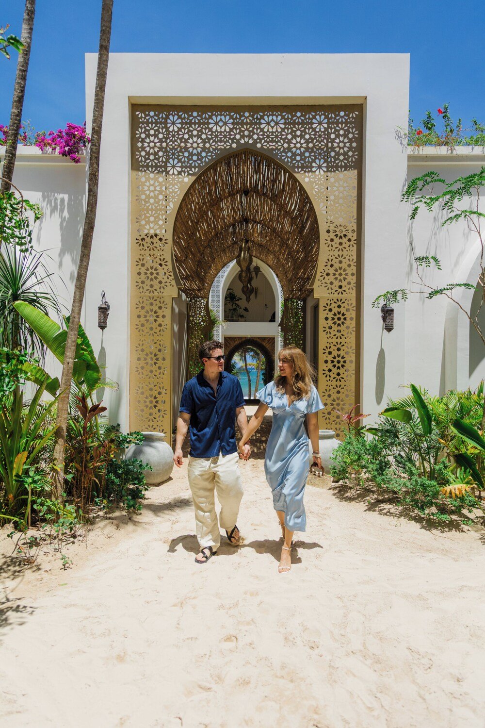 Pareja caminando por un sendero de arena hacia un edificio