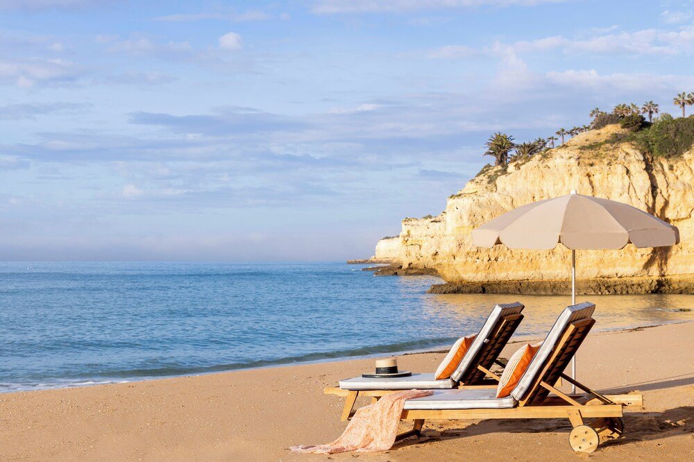 Playa con dos tumbonas bajo una sombrilla beige cerca del hotel